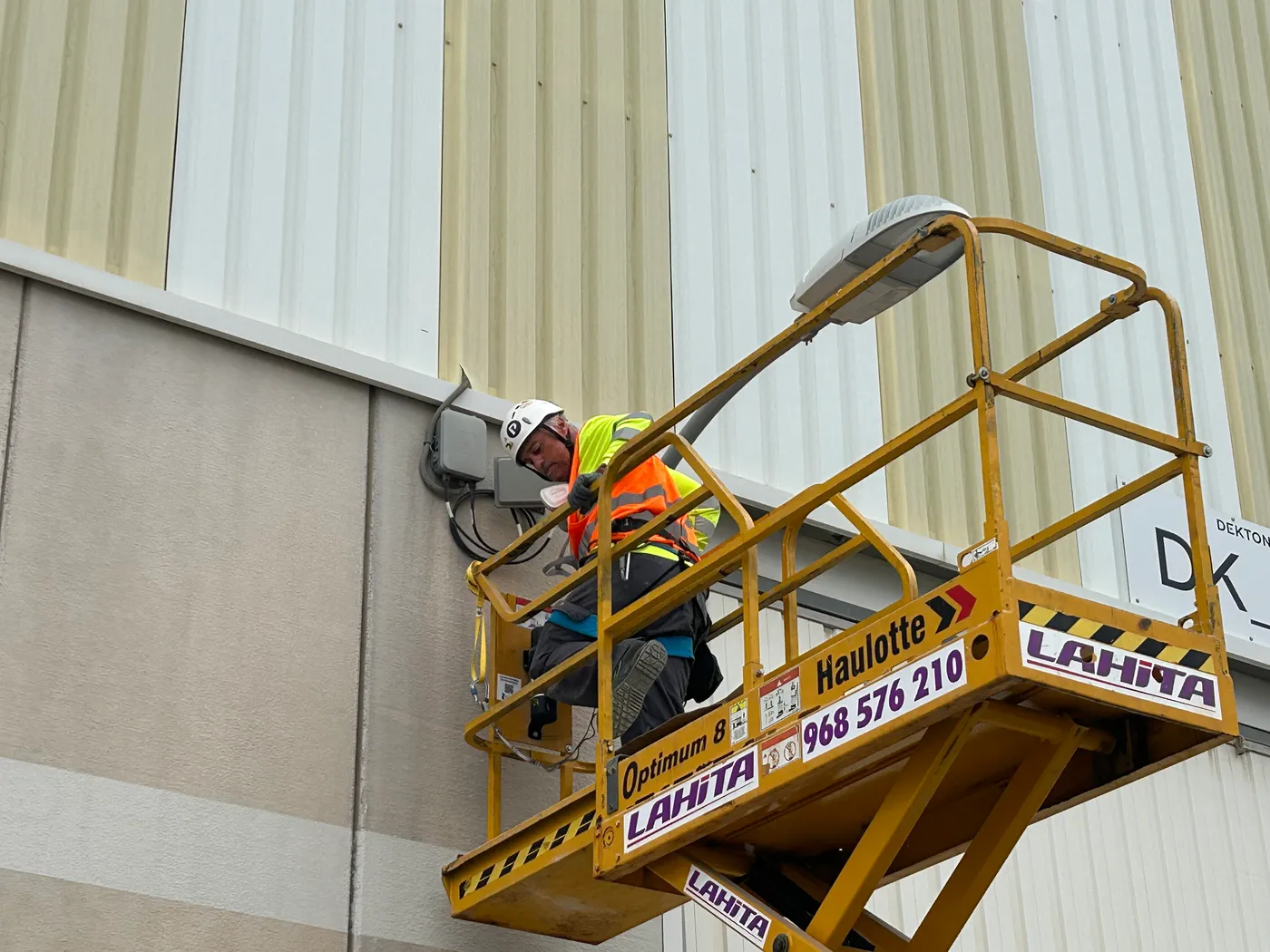 Detalle de técnico trabajando desde plataforma de tijera amarilla instalando equipo