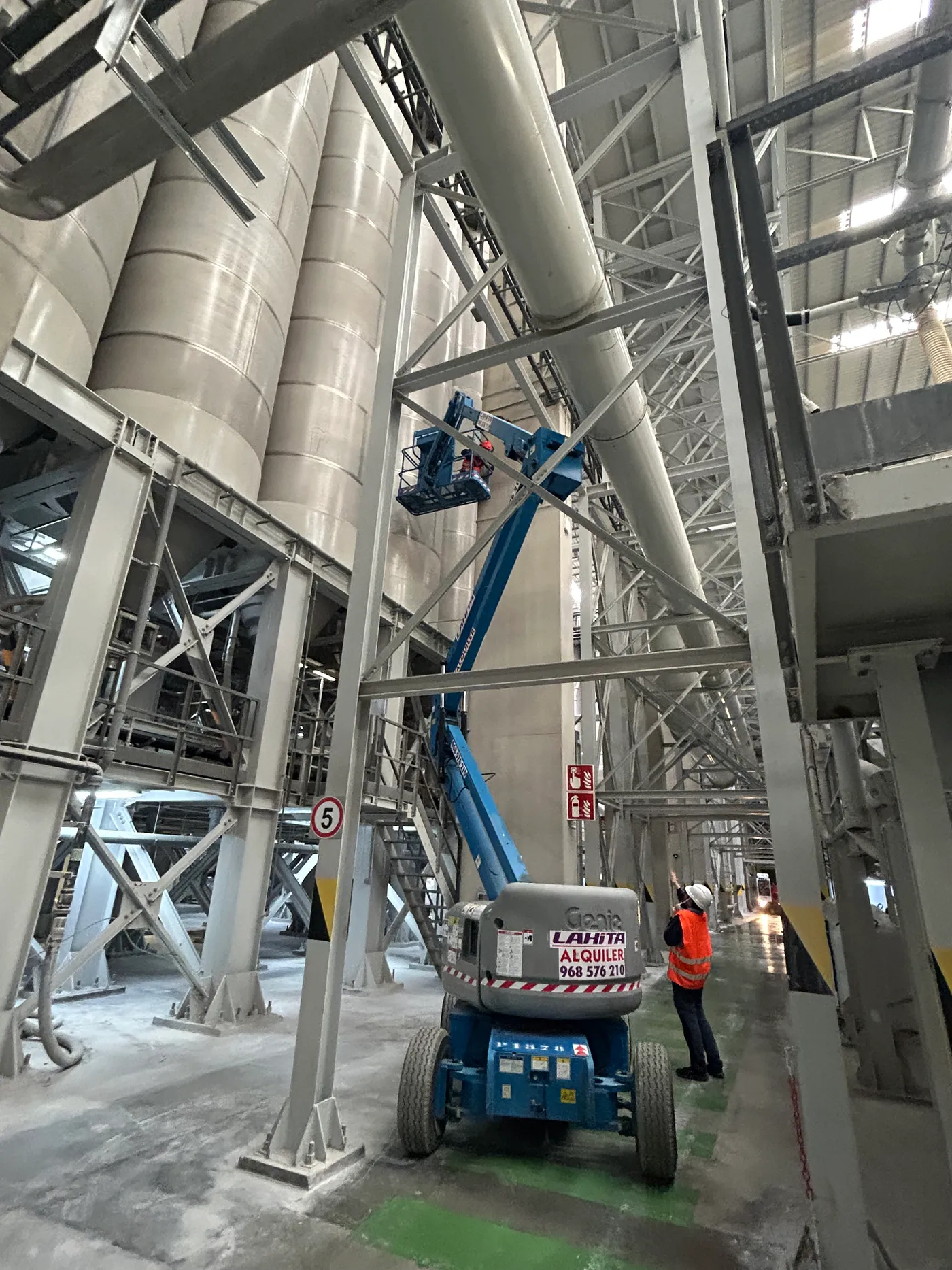 Plataforma elevadora trabajando en el interior de una nave industrial de gran altura entre silos